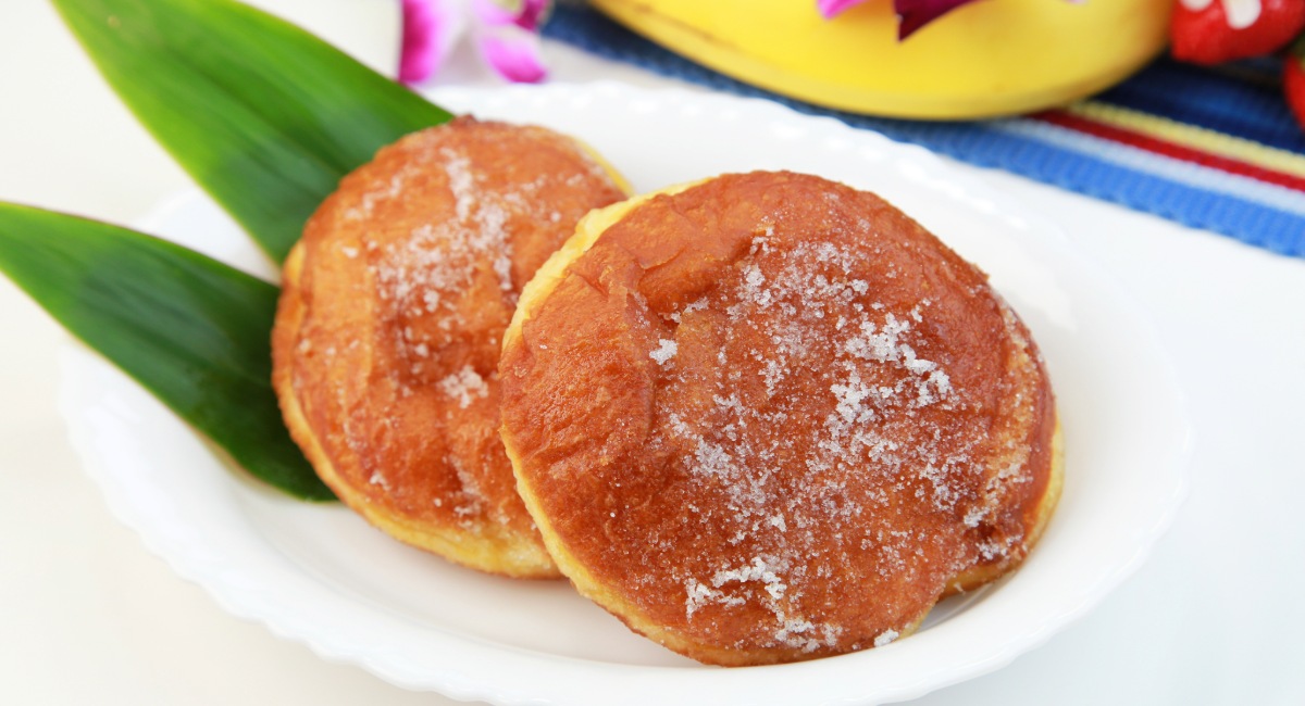 Sugar-dusted malasadas on a white plate with a ti leaf garnish, a specialty at Komoda Store & Bakery, a Makawao institution since 1916