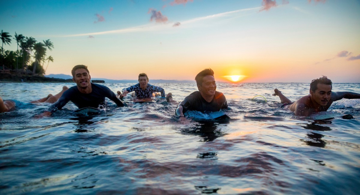 Group surf lesson participants floating on surfboards during golden hour sunset at Maui beach with instructor guidance