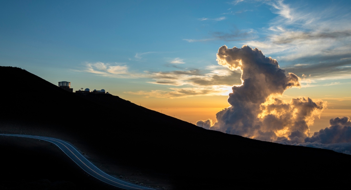 Pre-dawn sky above the Haleakala summit with golden clouds and a winding road on the mountain slope, Haleakala National Park, Maui