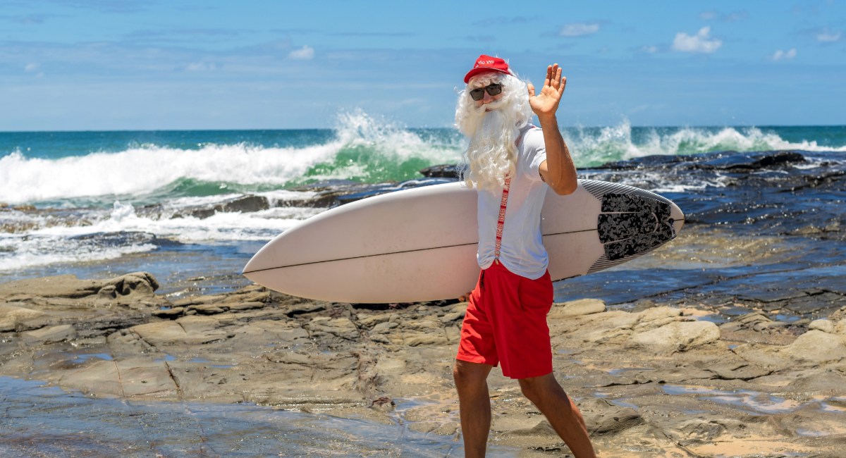 Santa Claus with surfboard on Maui Hawaii beach celebrating a tropical Christmas holiday
