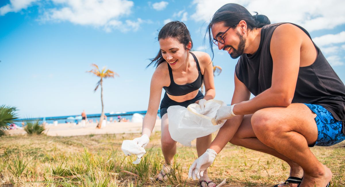 A man and a woman are picking up trash on a beach. They are both wearing gloves.